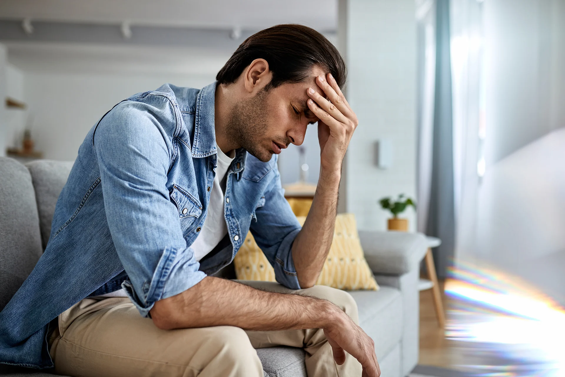 Ein Vater mit Depressionen hält sich den Kopf. Seine Augen sind geschlossen.